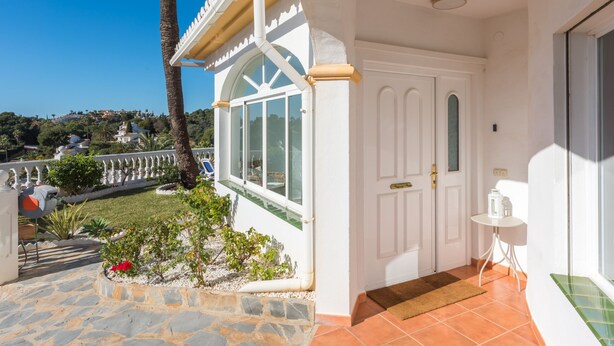A white building with a stone patio, a palm tree, and a view of a hillside. - Villa Panorama – Ocean View Oasis with Private Pool, Mijas Costa (Mijas Costa)