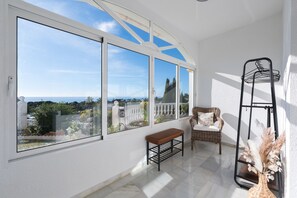 A sunlit room with large windows, a wicker sofa, a bench, and a metal shelf with dried flowers. - Villa Panorama – Ocean View Oasis with Private Pool, Mijas Costa (Mijas Costa)