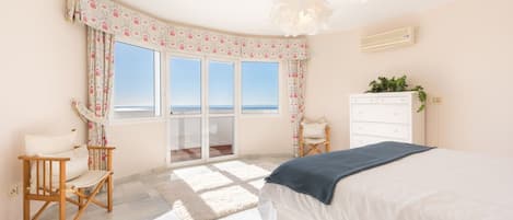 A bedroom with a bed, a dresser, a chair, a window with a view, and a balcony.