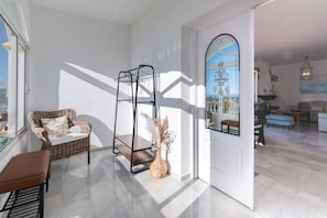 Una habitación luminosa con una silla de mimbre, una estantería metálica y un jarrón con flores secas.