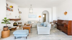A spacious living room with a sofa, ottoman, coffee table, and a piano. - Villa Panorama – Ocean View Oasis with Private Pool, Mijas Costa (Mijas Costa)
