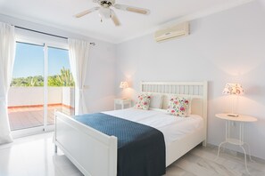 A bedroom with a bed, two bedside tables, a ceiling fan, and a view of the outdoors. - Villa Panorama – Ocean View Oasis with Private Pool, Mijas Costa (Mijas Costa)