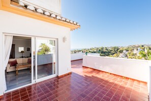 A balcony with red tiles, a sliding glass door, and a view of a hillside with greenery and buildings. - Villa Panorama – Ocean View Oasis with Private Pool, Mijas Costa (Mijas Costa)