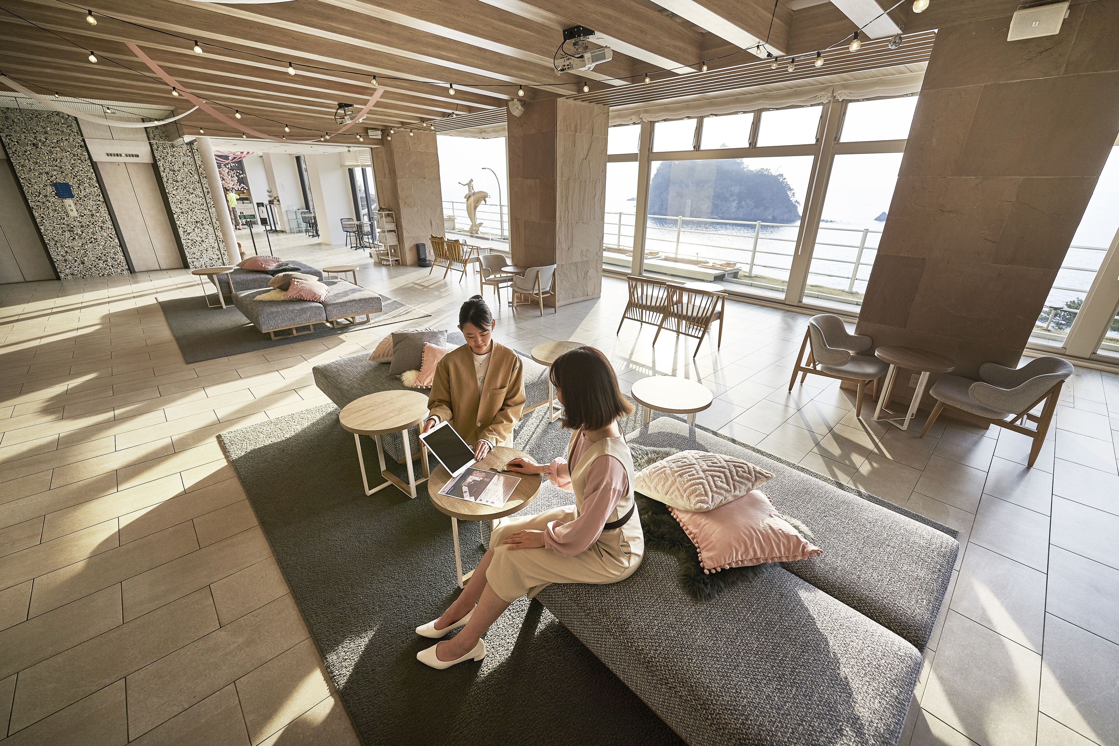 Un vaste espace salon aménagé avec des sièges confortables, une grande fenêtre offrant une vue dégagée et un plafond avec des poutres apparentes.
