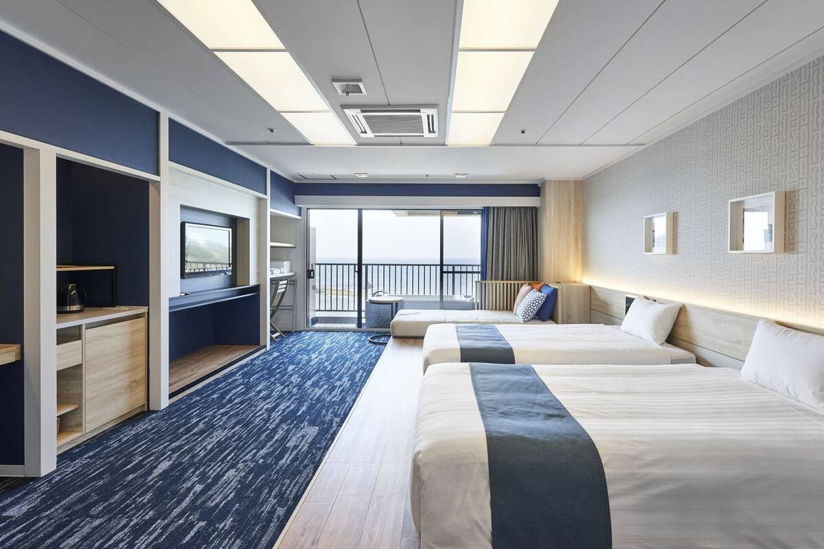 Ein Hotelzimmer mit Balkon, Schreibtisch, Bett und Fernseher.