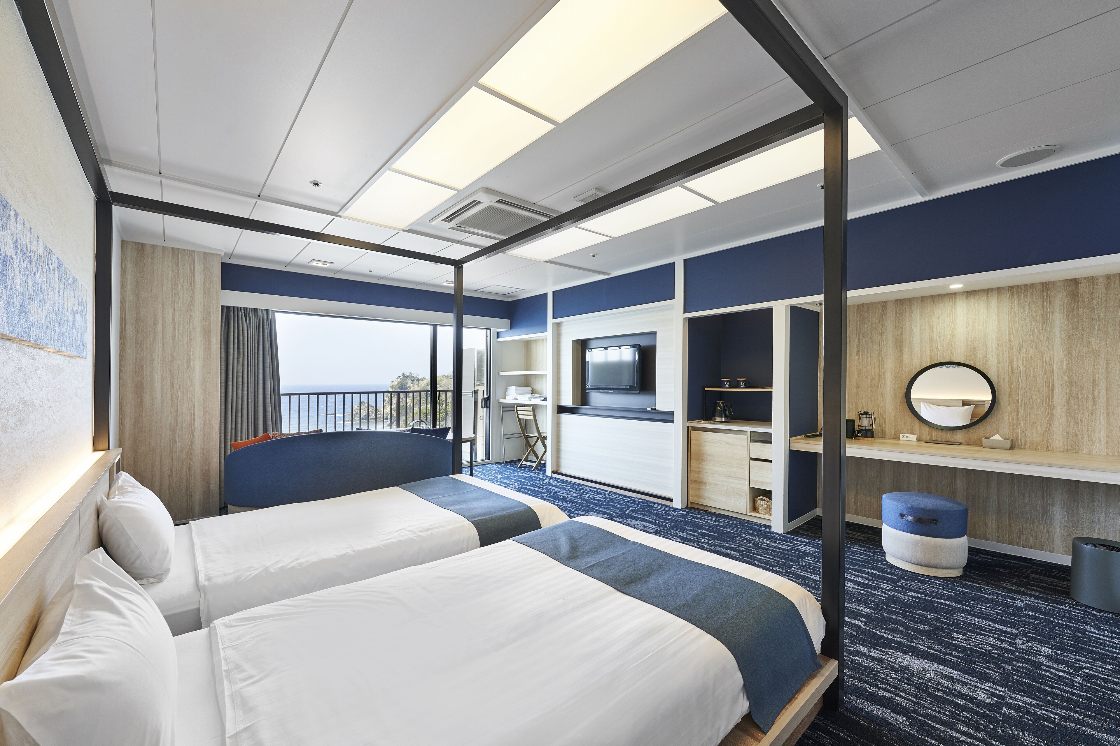Ein Hotelzimmer mit zwei Betten, einem Schreibtisch, einem Fernseher, einem Spiegel und einem Balkon mit Aussicht.