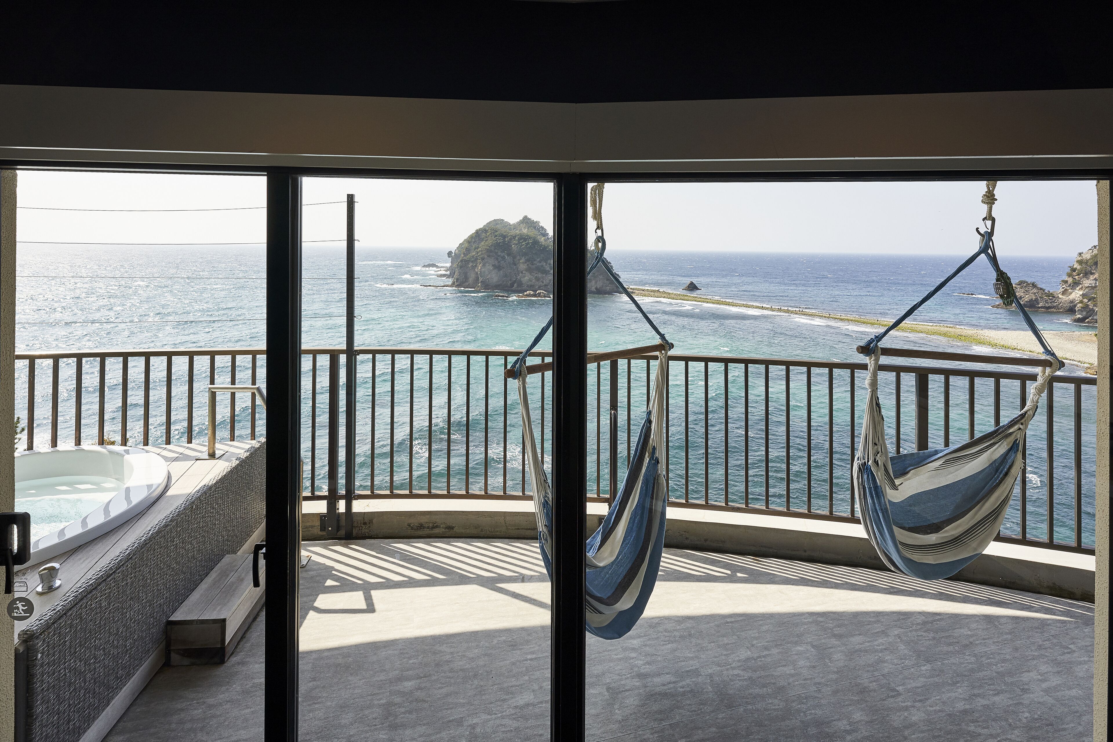 A balcony with a view of the sea, a hot tub, and two hammocks.
