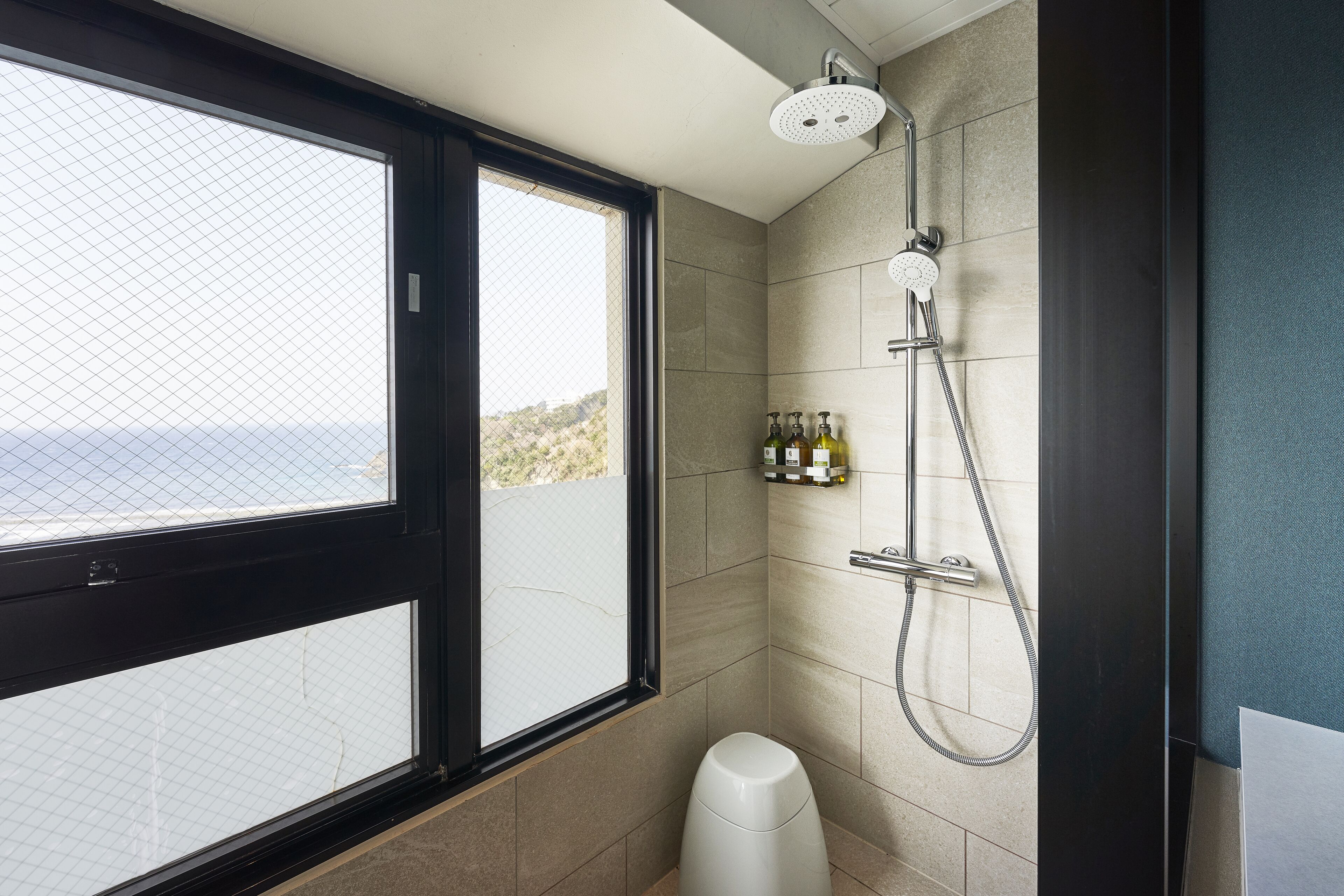 A modern bathroom with a large window, a shower, and a toilet.