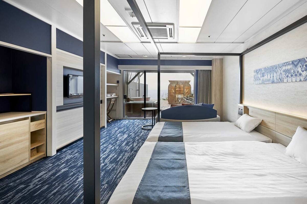 Ein Hotelzimmer mit einem Bett, Nachttischen, einem Schreibtisch, einem Sessel und einem Blick ins Freie.