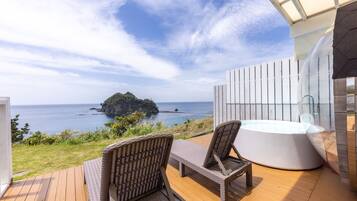 A balcony with wicker chairs, a hot tub, and a view of the sea and a small island.