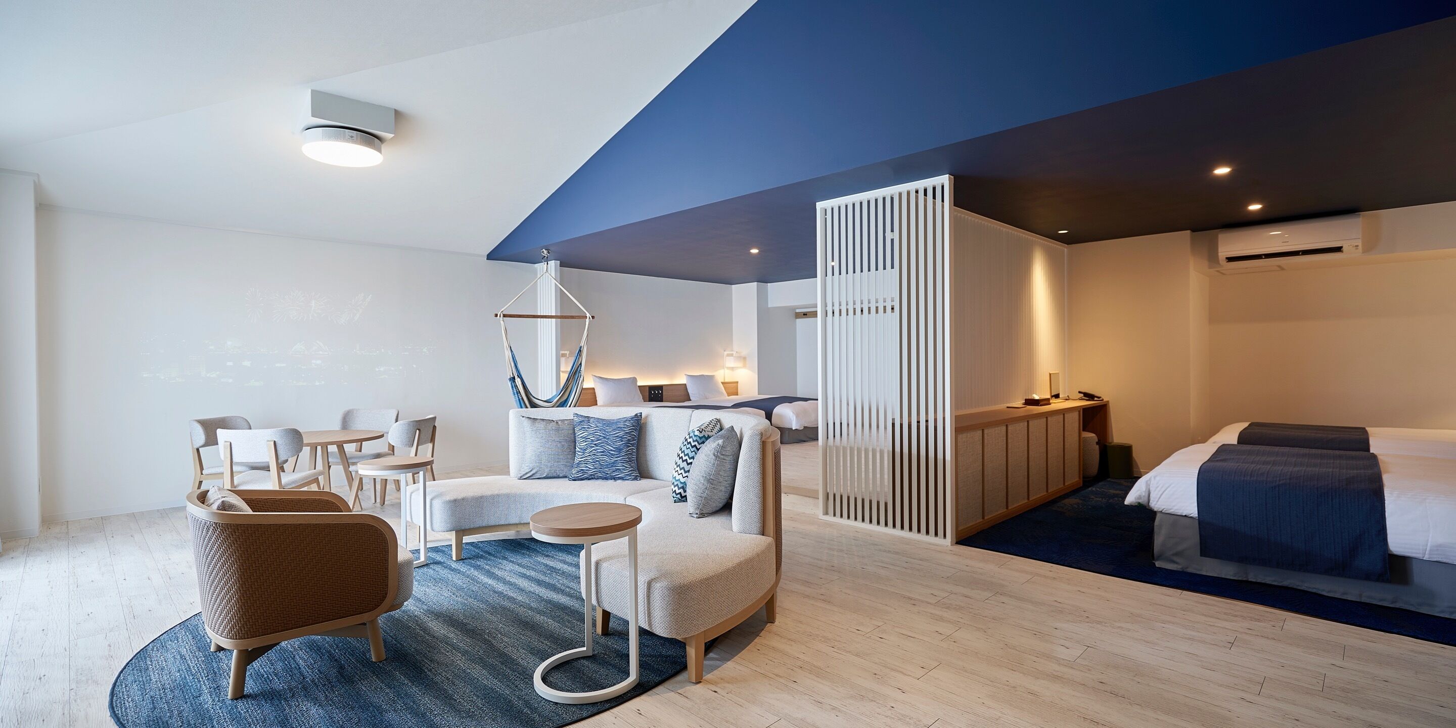 A modern hotel room with a sofa, chairs, a small table, a bed, and a partition wall.