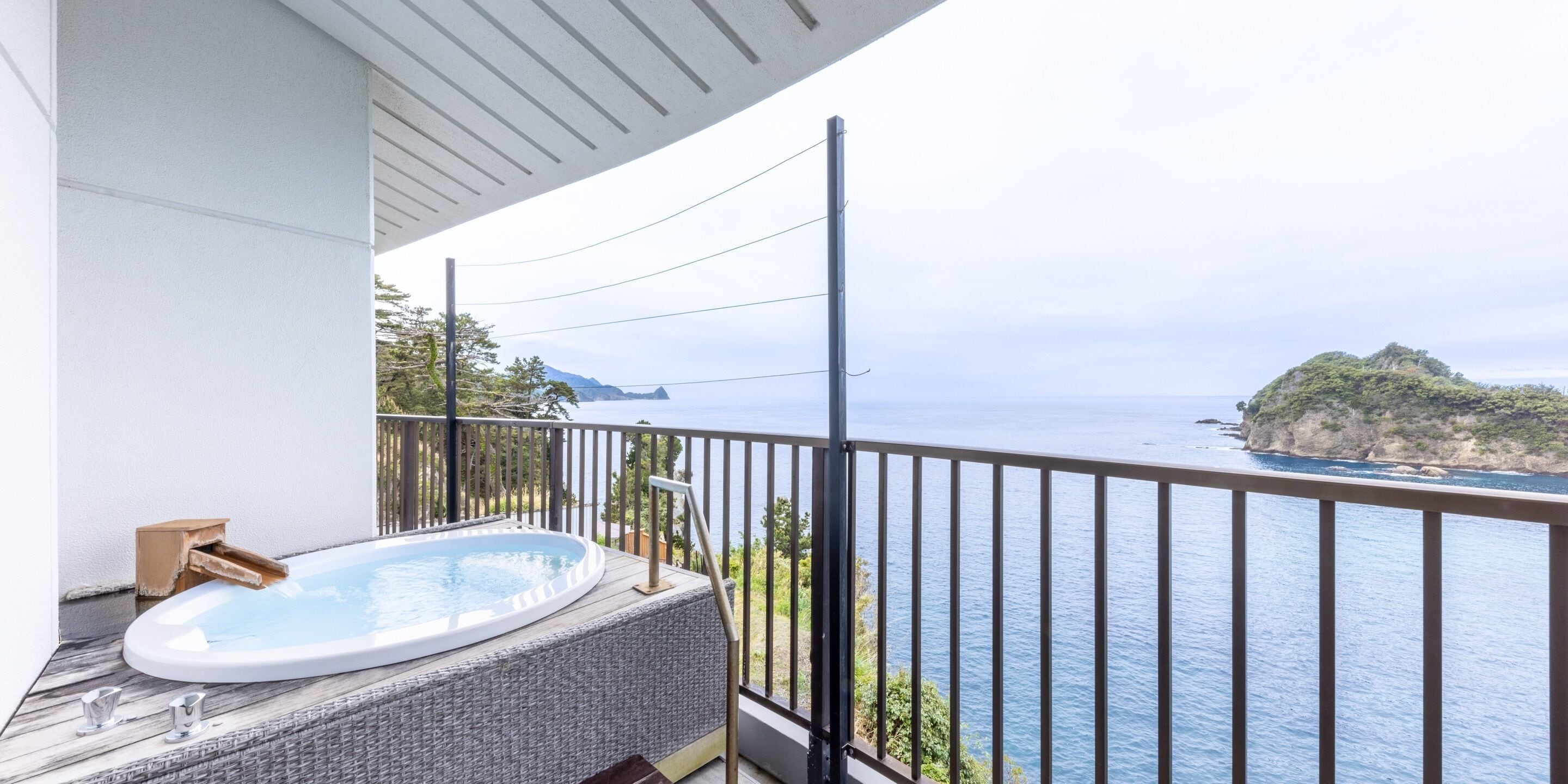 Un balcón con un jacuzzi, vistas al mar y un paisaje montañoso.