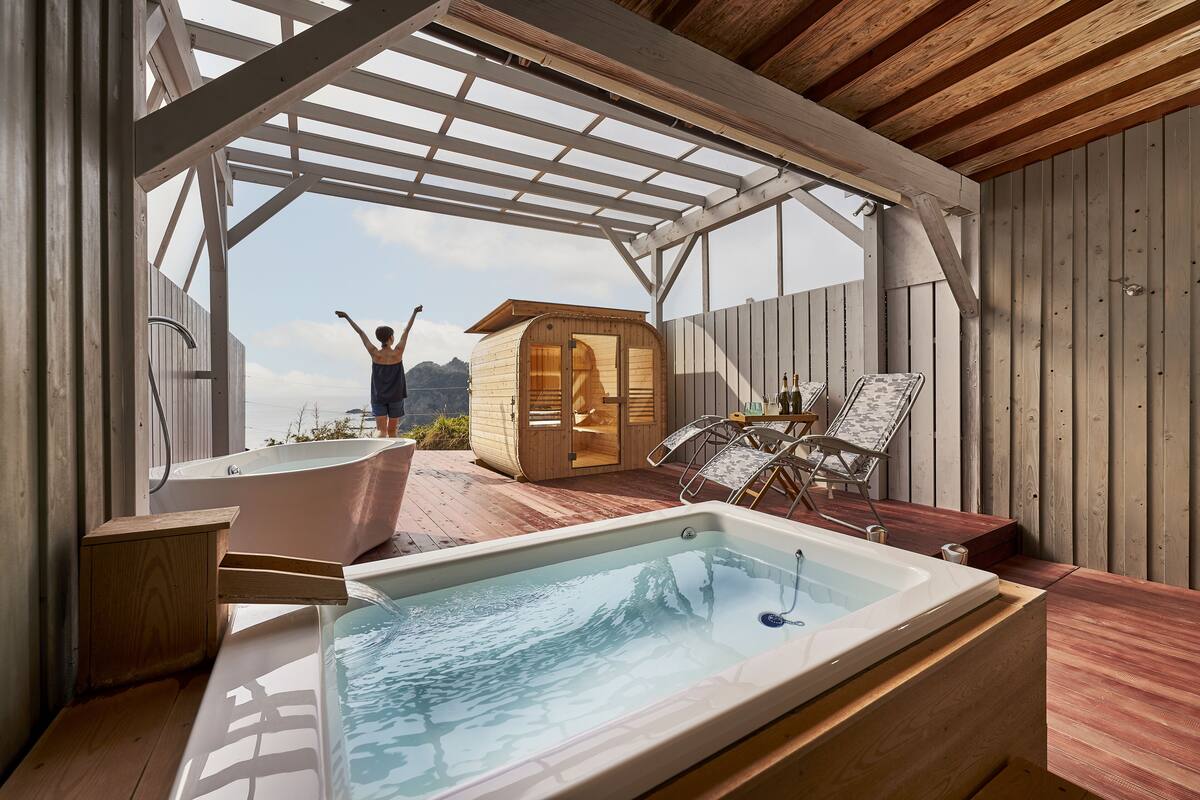 Eine Holzterrasse mit Whirlpool, Holzzause und einer Liege.