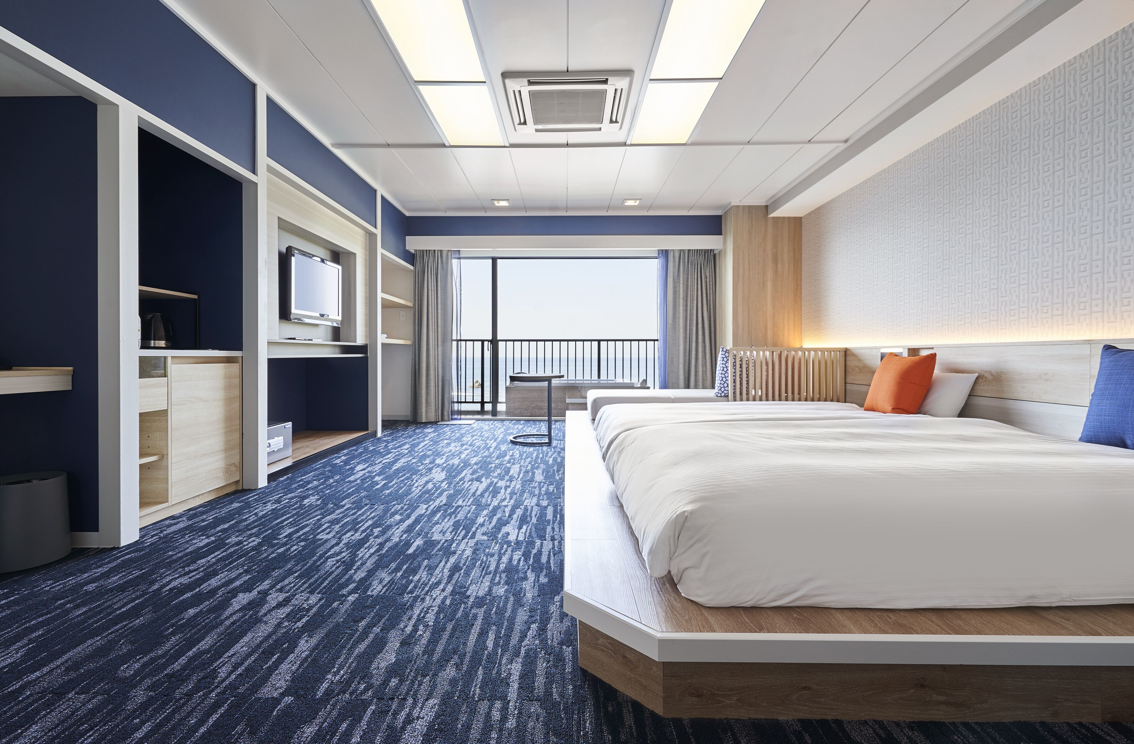 Quarto de hotel com uma cama grande, uma escrivaninha, uma cadeira, uma TV e vista para o exterior.