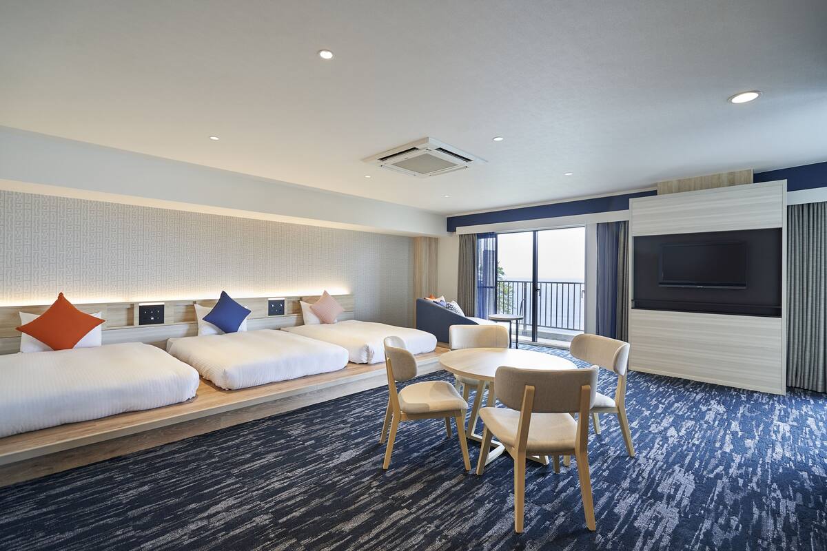 Ein Hotelzimmer mit einem großen Bett, einem Esstisch mit Stühlen, einem Fernseher und einem Balkon mit Aussicht.