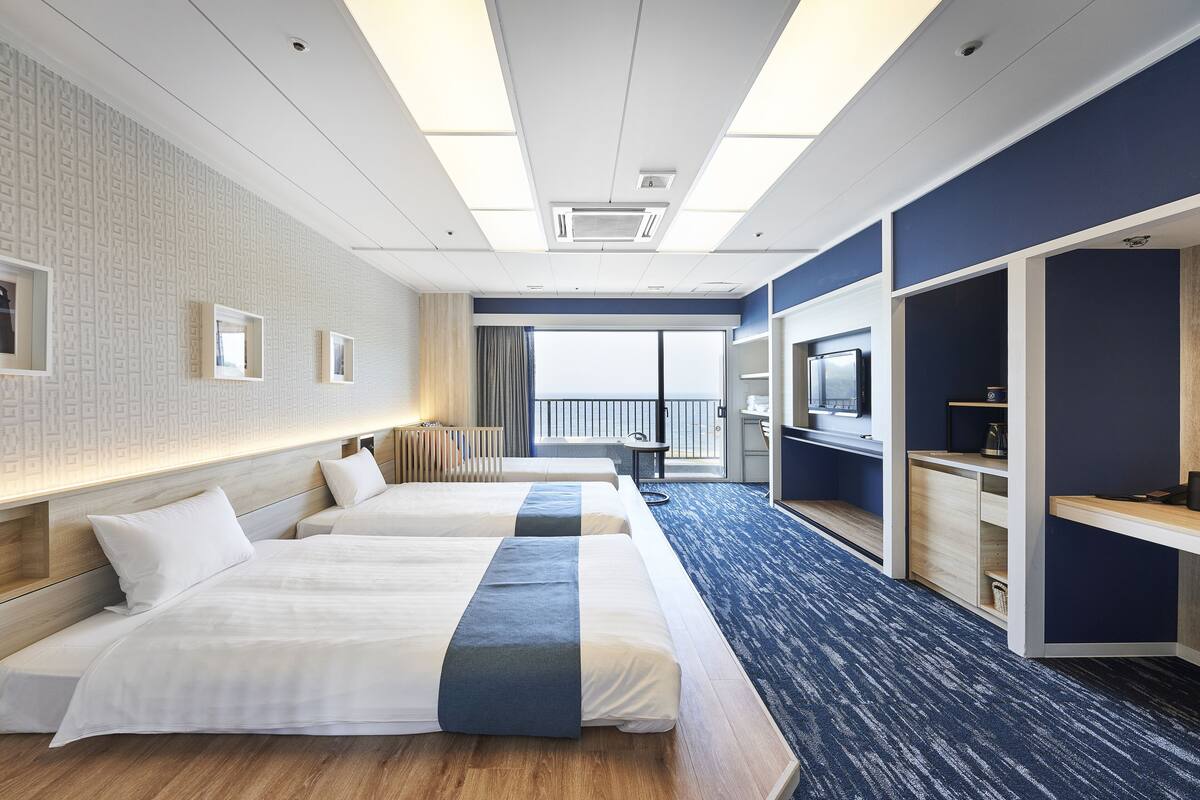Ein Hotelzimmer mit zwei Betten, einem Schreibtisch, einem Fernseher und Blick ins Freie.