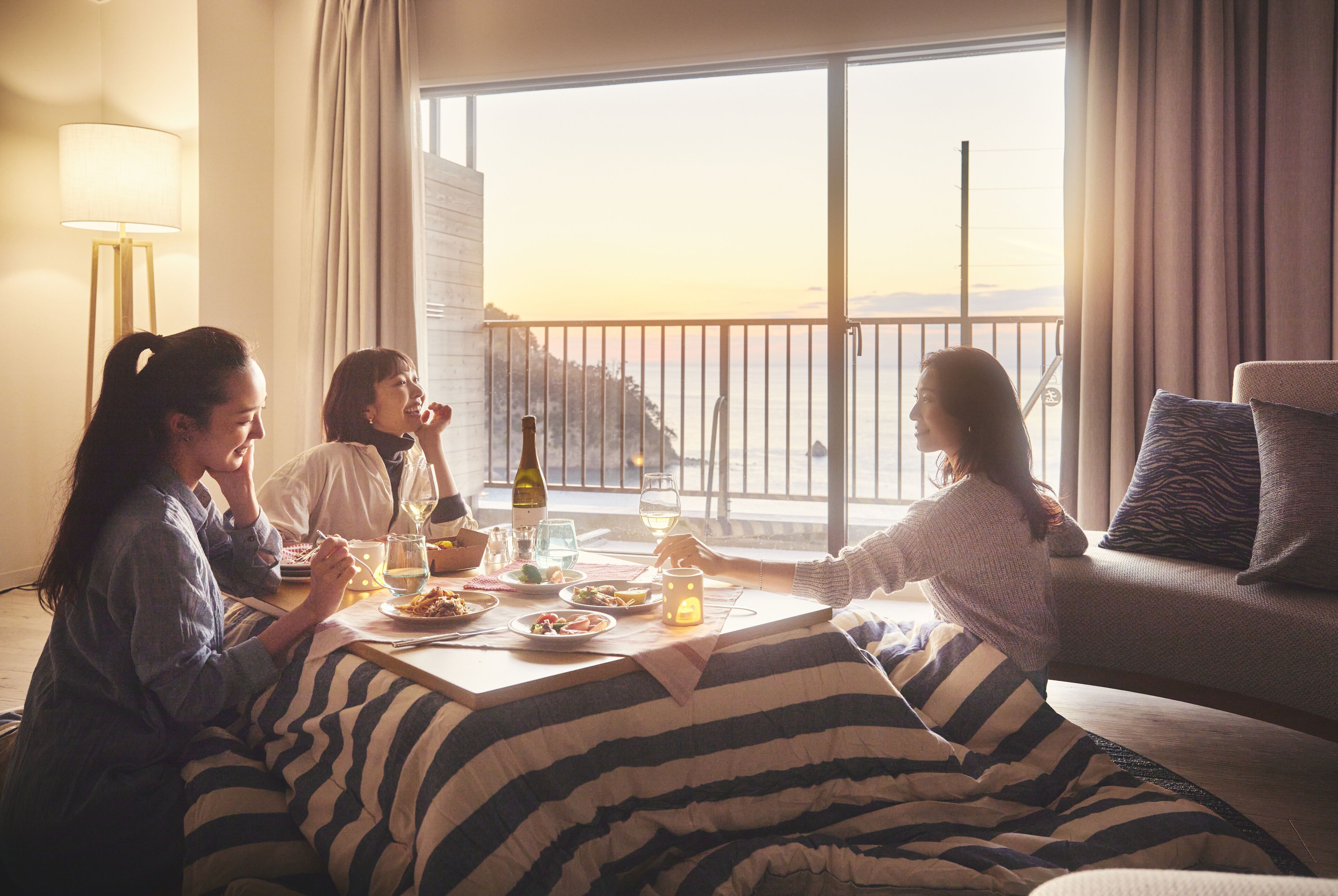 Un comedor con una mesa dispuesta para tres personas, un sofá y vistas al mar a través de amplias ventanas.