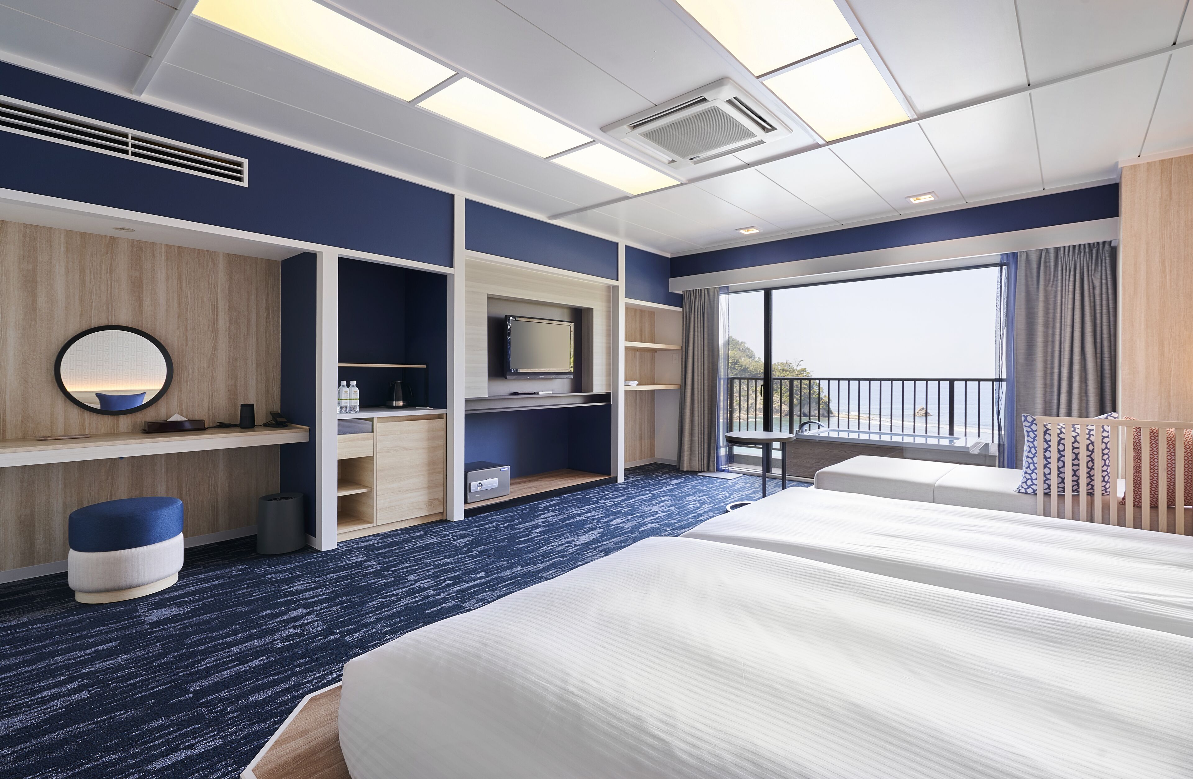 Een moderne hotelkamer met een groot bed, een bureau met een flatscreen televisie, inbouwplanken, een balkon met uitzicht en een groot raam.