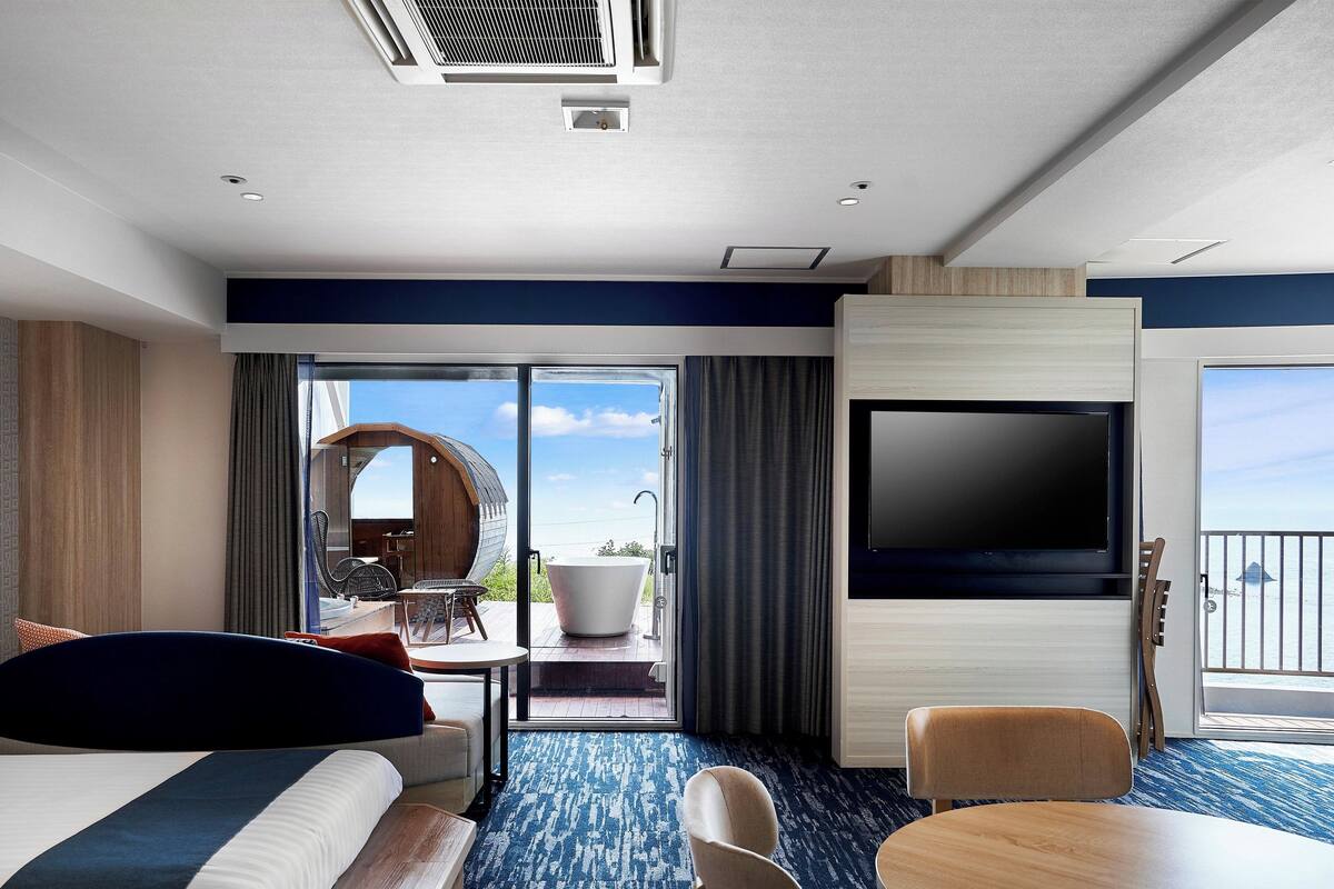 Ein modernes Hotelzimmer mit einem großen Bett, einem Flachbildfernseher, einem Balkon mit Aussicht und einem Essbereich.