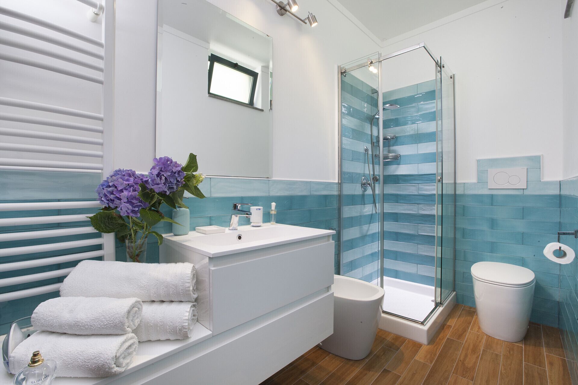 Une salle de bain moderne avec une douche à l’italienne en verre, un lavabo blanc et un grand miroir.