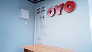 A room with a wooden desk, a white door, and a wall with the letters "OYO" in red. - OYO 1007 Alletha Guest House 2 (Balikpapan)
