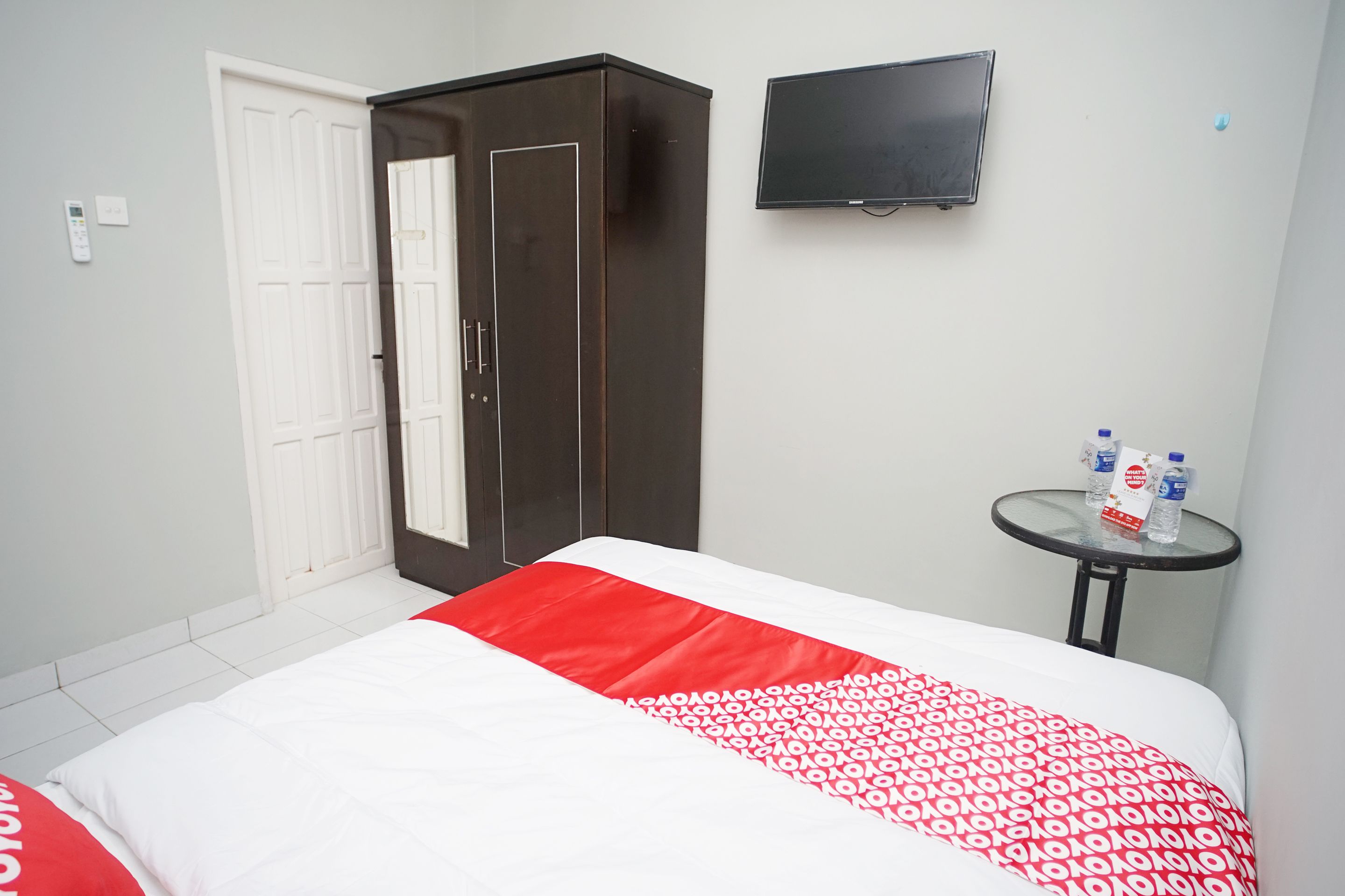 A hotel room with a bed, a wardrobe, a TV, and a small table with water bottles.