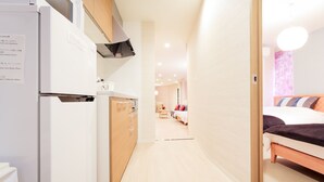 Een moderne hotelkamer met kitchenette, een bed met donkere deken en uitzicht op de gang naar de ontbijtruimte.