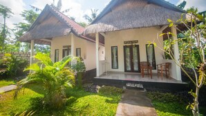 Un edificio de estilo bungalow con techo de paja, un porche cubierto y un pequeño jardín con palmeras.