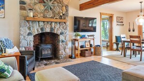 A cozy living room with a stone fireplace, a television, and a dining area with wooden furniture. - Burt Lake Waterfront Lakehouse (Indian River)