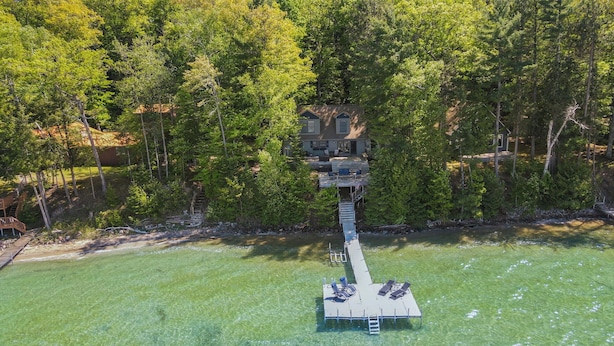 A house with a dock extending into a lake, surrounded by dense forest. - Burt Lake Waterfront Lakehouse (Indian River)