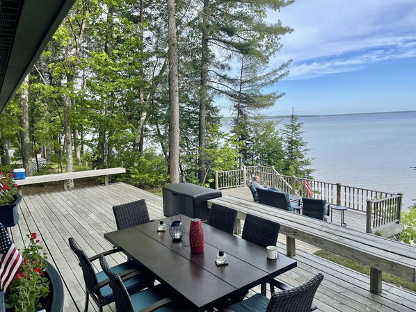 A wooden deck with a table and chairs, overlooking a body of water and surrounded by trees.