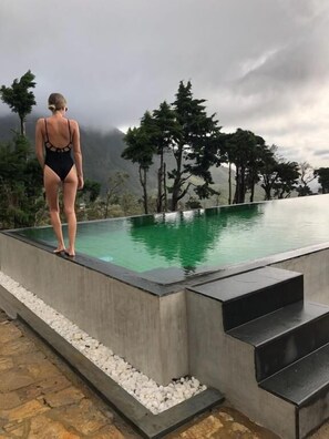 Una persona al costat de la piscina, amb vista a arbres i muntanyes al fons.