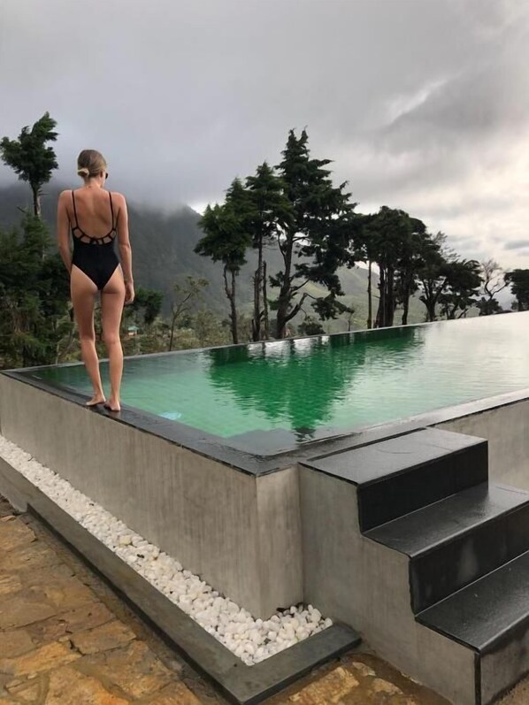 A person standing at the edge of a pool with a view of trees and mountains in the background. - Tea & Experience Factory (HANGURANKETHA)