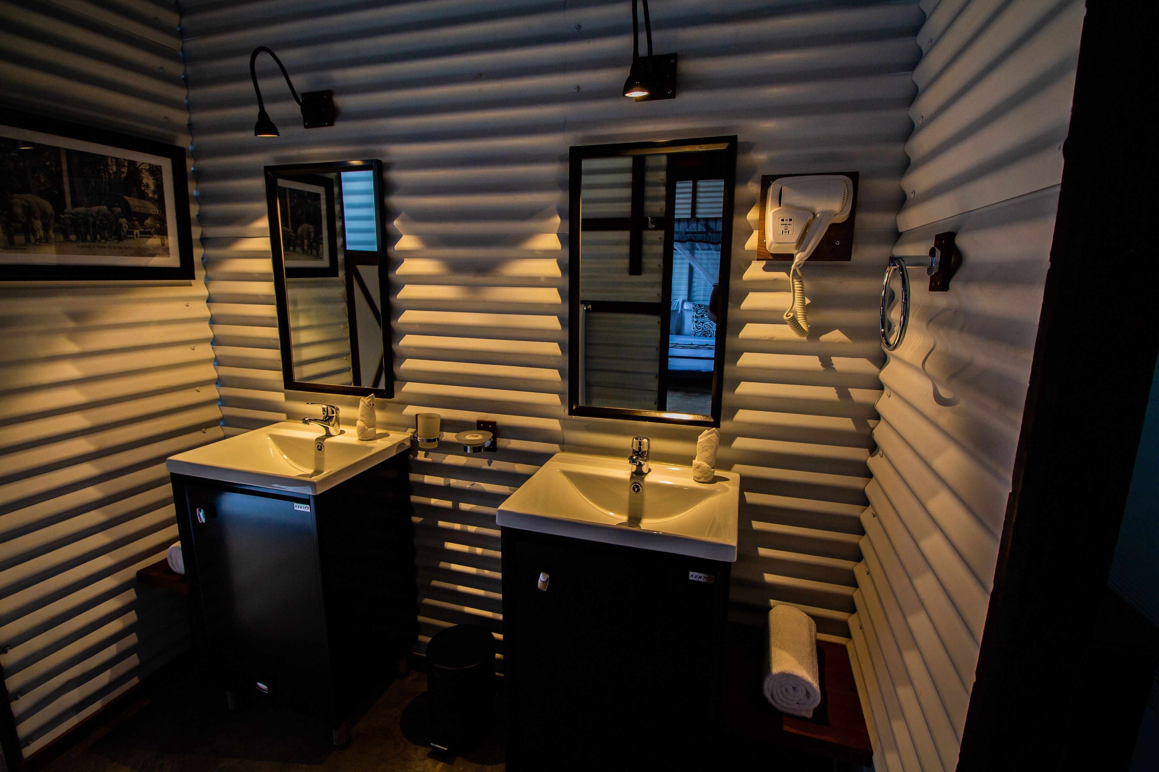 A bathroom with two sinks, a mirror, a towel dispenser, and a toilet.
