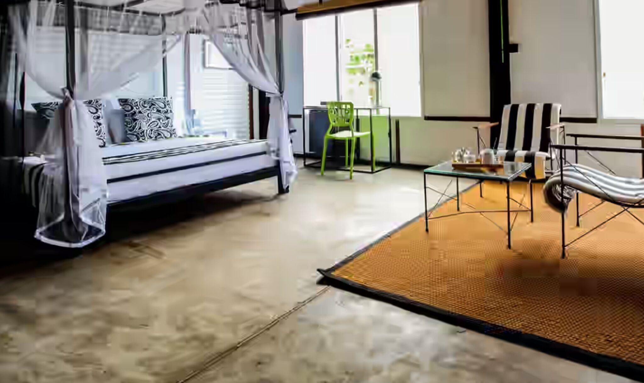 A room with a bed, a green chair, a table, and a view of the outdoors.