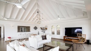 Ein geräumiges Wohnzimmer mit hohen Decken, weißen Sofas, einem Couchtisch und einem Fernseher.