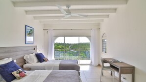 Ein Schlafzimmer mit zwei Betten, einem Schreibtisch und einem großen Fenster mit Blick auf Grünflächen.