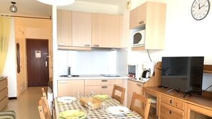 Ett kompakt kök med träskåp, en mikrovågsugn, en kaffebryggare och en tv placerad på ett träställ.