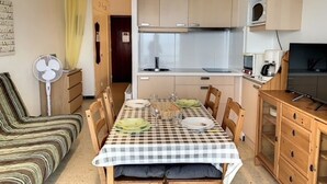 Ett kompakt kök med ett matbord för fyra personer, en soffa och en tv.