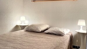 En snyggt bäddad säng med ett beige överkast och två kuddar, med två sängbord med lampor på var sin sida, i ett rum med väggar med en tydlig struktur och en sänggavel i trä.