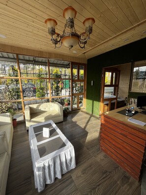 A cozy room with a wooden ceiling, a sofa, a coffee table, and a reception desk. - Mosaic Go, Chail  (Shimla)