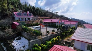 A hotel with multiple buildings, a parking area, and a mountainous backdrop. - Mosaic Go, Chail  (Shimla)