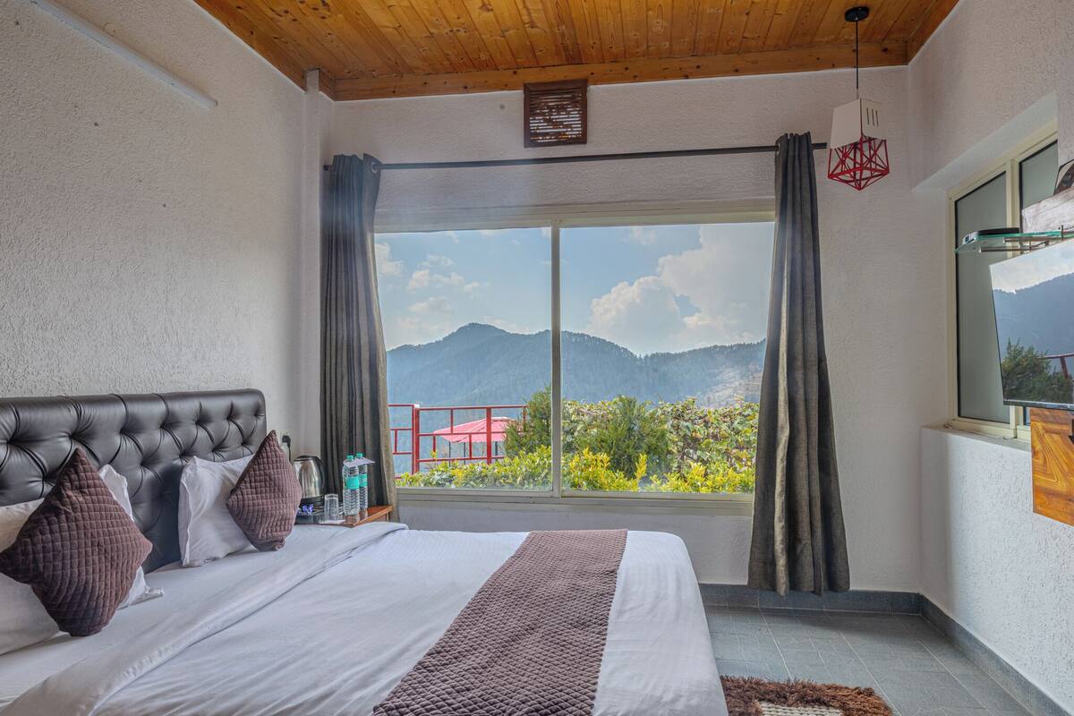 A bedroom with a large bed, a view of mountains, and a wooden ceiling.
