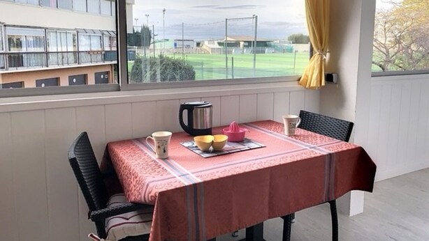 Ein Balkon mit Tisch für zwei Personen, einem Wasserkocher und Blick auf ein Sportfeld.