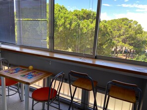 Une salle de classe dotée d’une grande fenêtre, d’une table en bois sur laquelle sont disposés du matériel pédagogique, et de trois chaises.