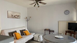 Una sala de estar con sofá, mesa de comedor, sillas, ventilador de techo, reloj y televisor.