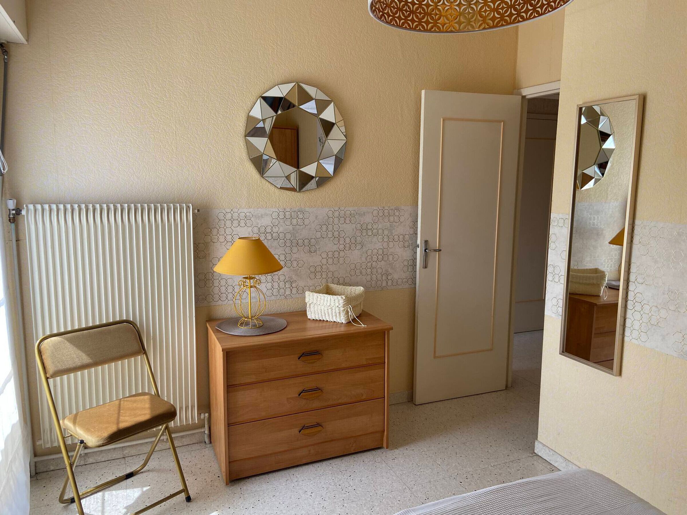 A room with a radiator, a wooden dresser with drawers, a chair, and a mirror on the wall.