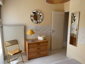 Een kamer met een radiator, een houten dressoir met lades, een stoel en een spiegel aan de muur.