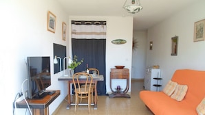 Een woonkamer met een oranje bank, een eethoek met een tafel en stoelen, een televisie en een keuken met kastjes en een spoelbak.