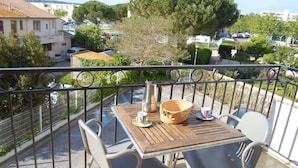Een balkon met een houten tafel en twee stoelen, met uitzicht op een parkeerplaats en gebouwen.